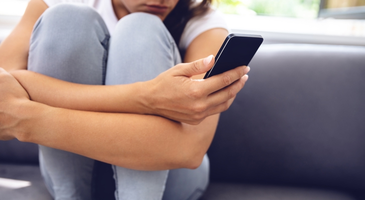 Kvinde sidder på sofa med telefon i hånden og oplever digitale krænkelser