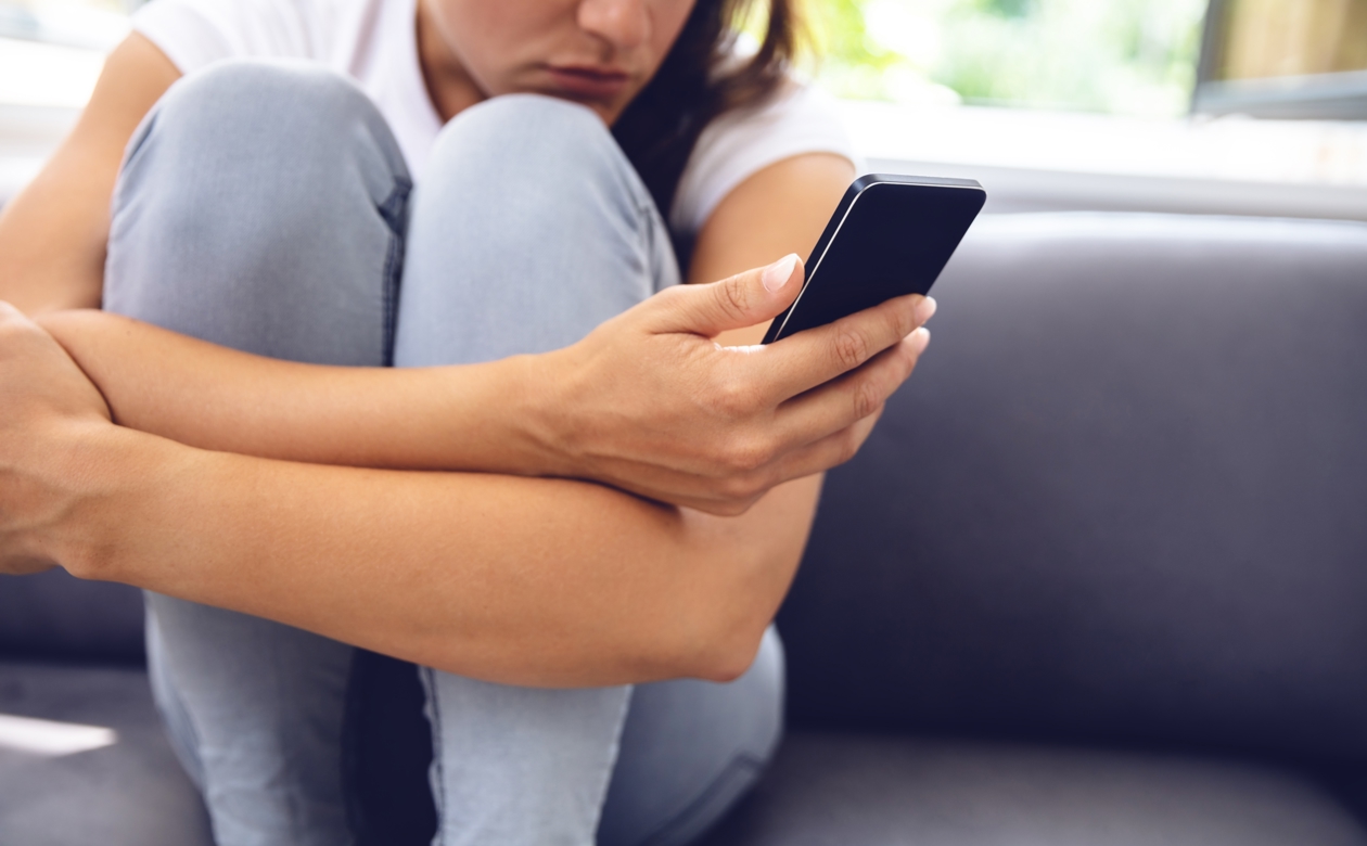 Kvinde sidder på sofa med telefon i hånden og oplever digitale krænkelser