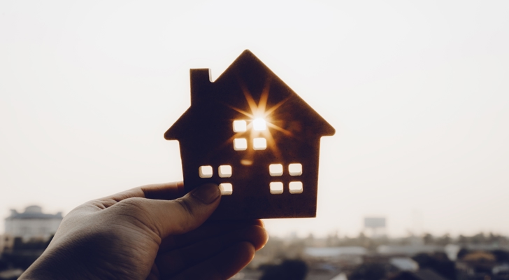 Hånd der holder et lille hus, hvor solen går igennem et af vinduerne