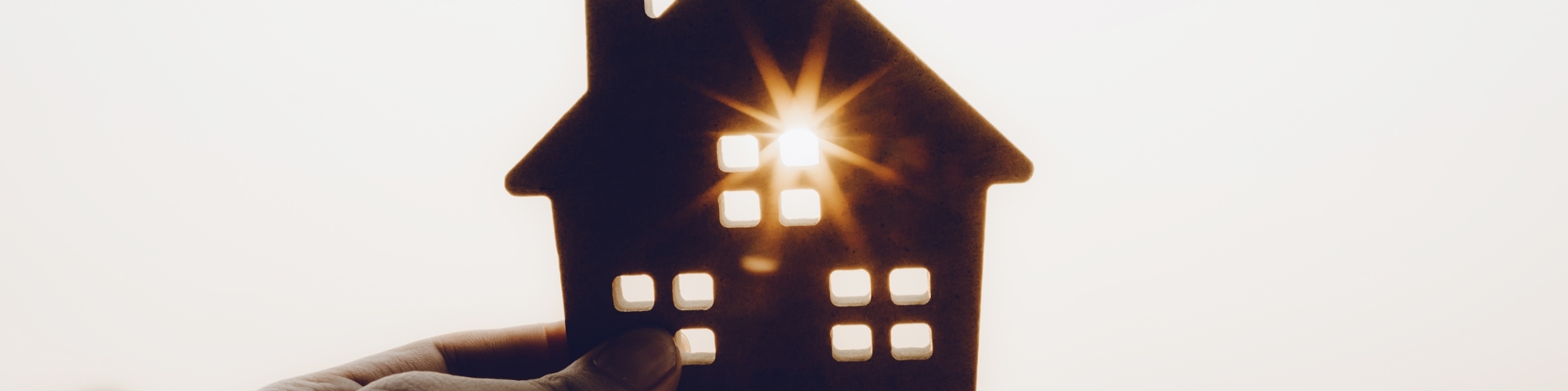 Hånd der holder et lille hus, hvor solen går igennem et af vinduerne