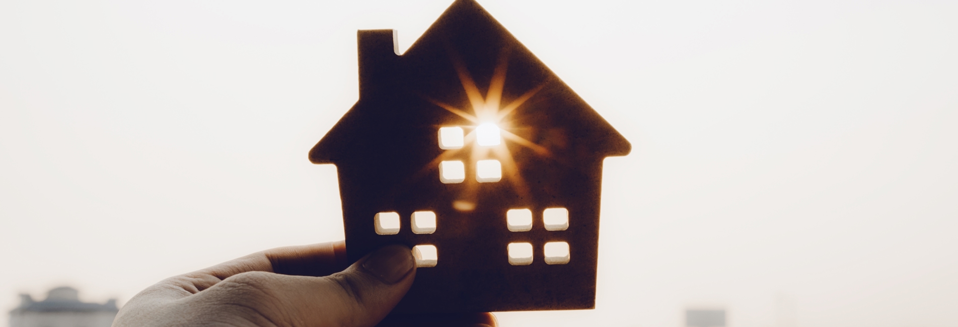 Hånd der holder et lille hus, hvor solen går igennem et af vinduerne