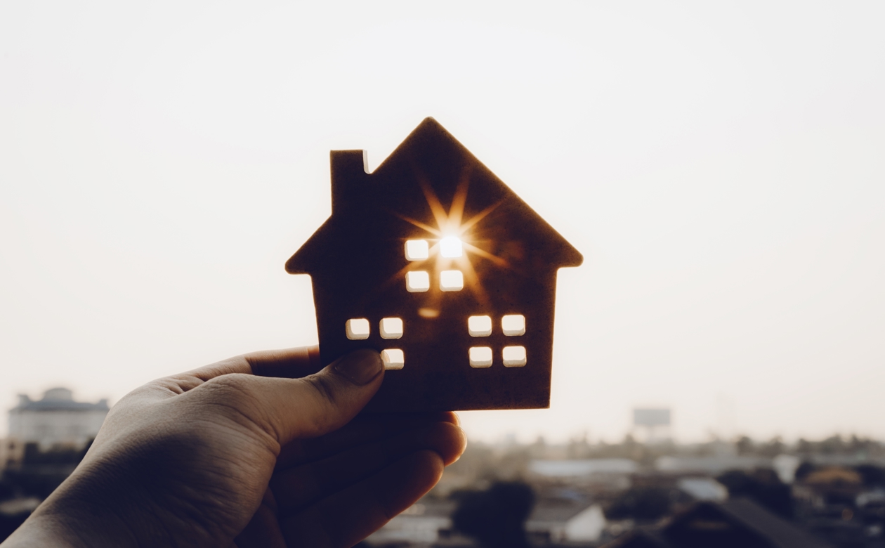 Hånd der holder et lille hus, hvor solen går igennem et af vinduerne