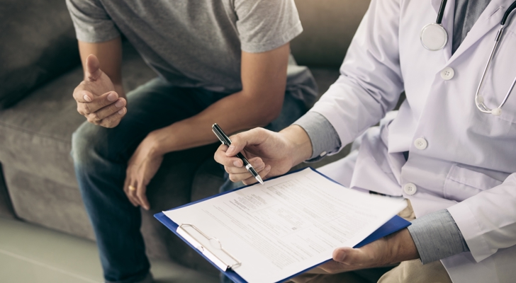 Læge og patient sidder på sofa og læge udfylder dokumenter med henblik på sygedage