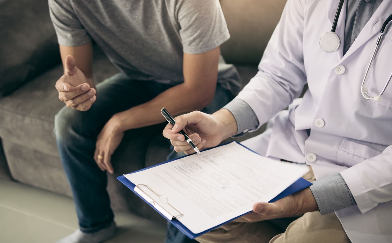 Læge og patient sidder på sofa og læge udfylder dokumenter med henblik på sygedage