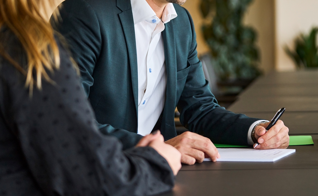 To personer i møde, hvor der bliver skrevet ned på papir af den ene