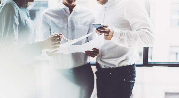 Tre personer står med papirer