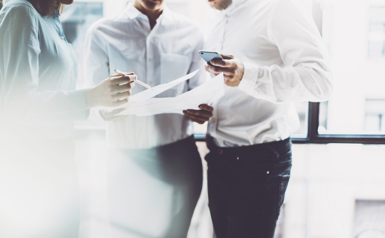 Tre personer står med papirer