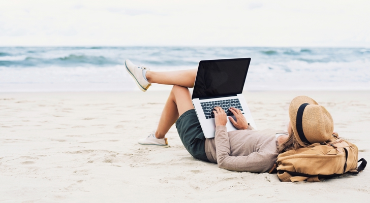 Kvinde ligger på stranden med sin computer på benene 