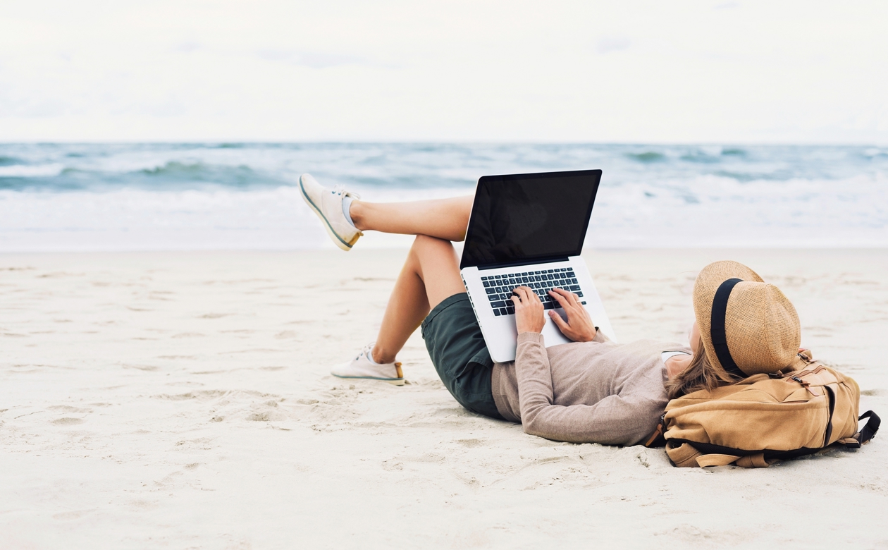 Kvinde ligger på stranden med sin computer på benene