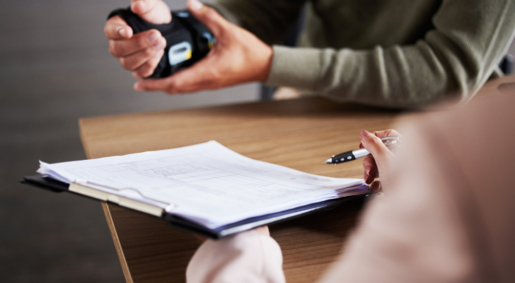 Kvinde sidder med papirer overfor en mand med hånden i en skinne grundet arbejdsskade