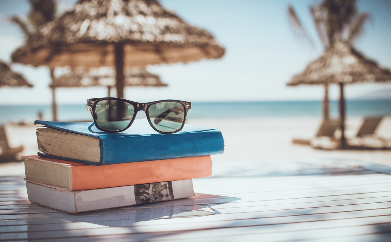 Solbriller ovenpå tre bøger med strand i baggrunden