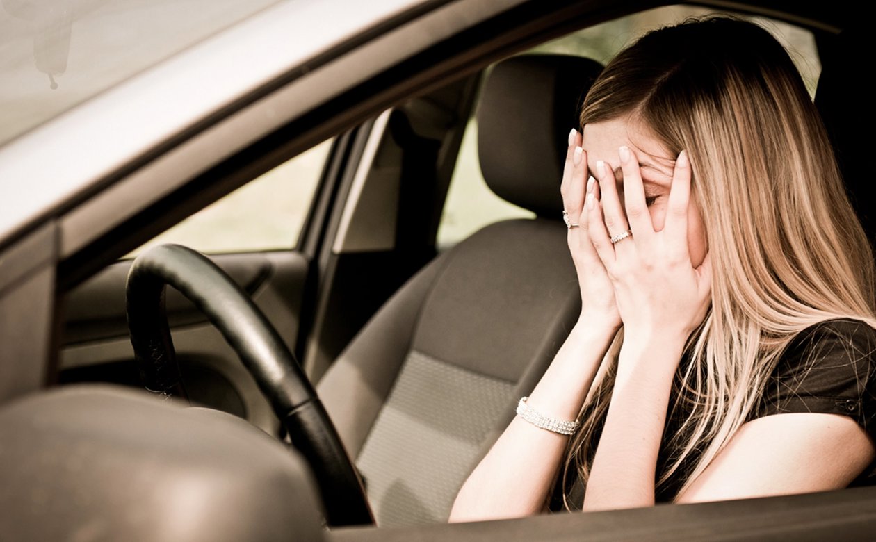 Kvinde sidder i bil og tager sig til hovedet