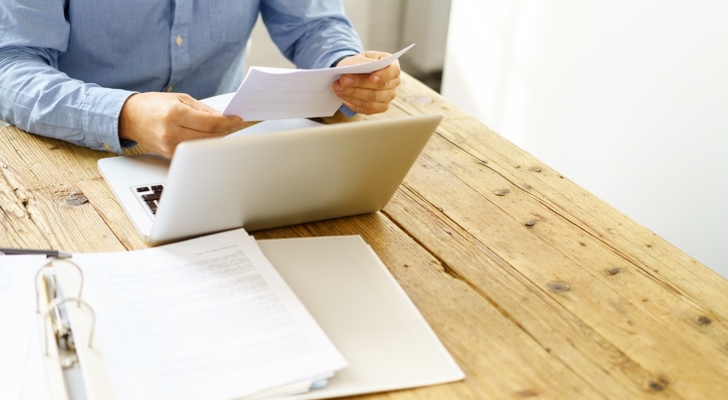 Mand arbejder ved computer og gennemgår papirdokumenter