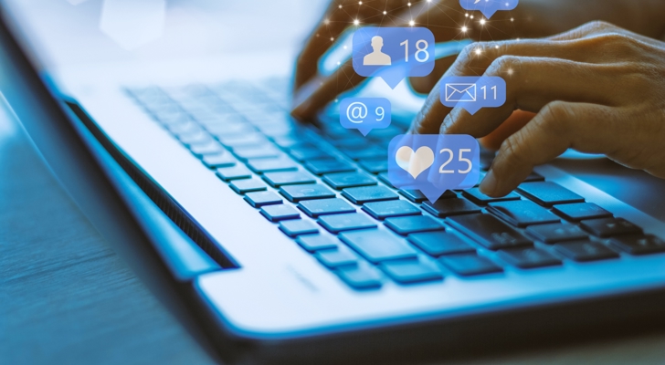 Hænder der taster på tastatur, hvor sociale medier hænger over