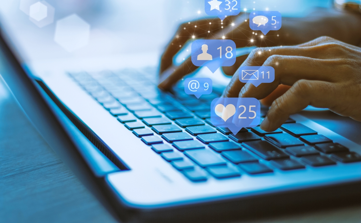 Hænder der taster på tastatur, hvor sociale medier hænger over