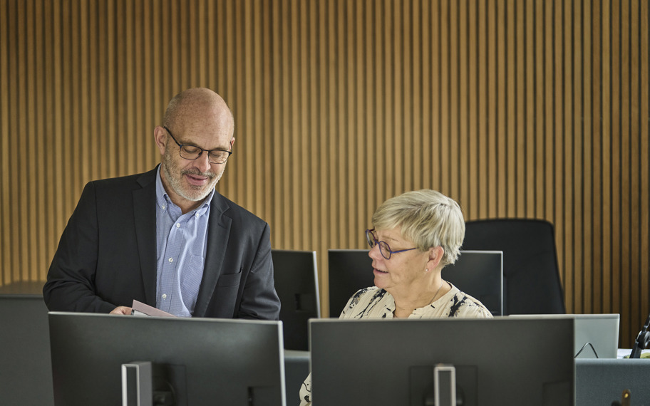 To kollegaer snakker sammen, hvor den ene sidder ved computer