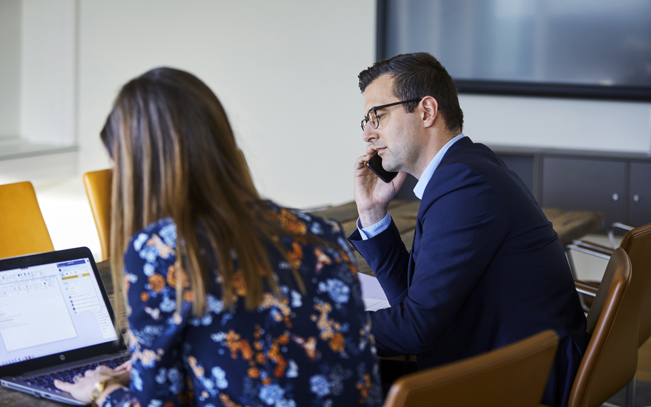 To advokater i Hjulmandkaptains Inkassoafdeling sidder ved et bord. Den ene taler i telefon og den anden ved computer