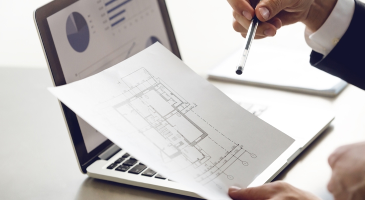 Person sidder ved computer og gennemgår plantegninger på papir
