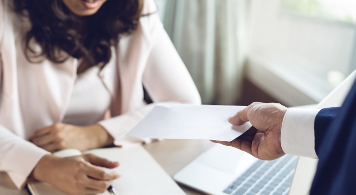Mand overrækker en seddel til kvinde, som sidder ved skrivebord