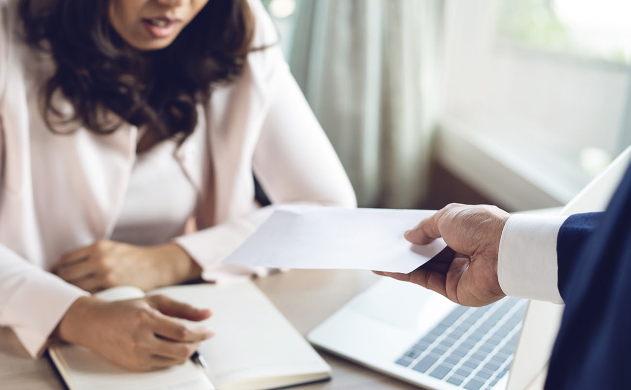 Mand overrækker en seddel til kvinde, som sidder ved skrivebord