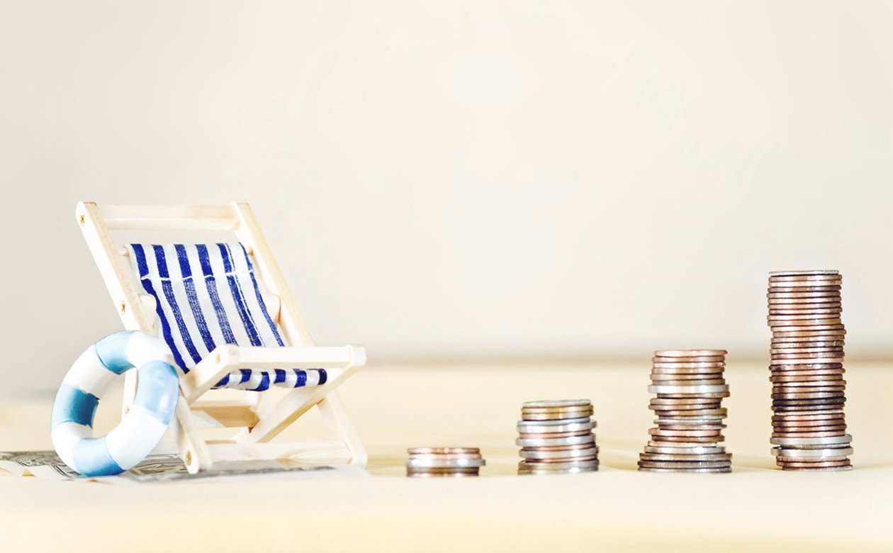 Stakke af mønter med lille strandstol med siden af - feriepenge