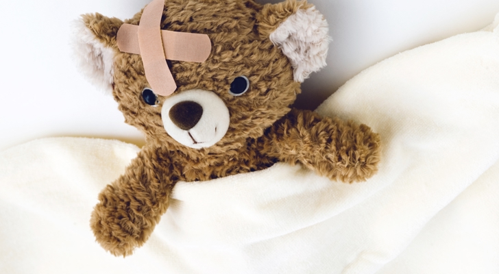 Bamse ligger under tæppe med et plaster i panden