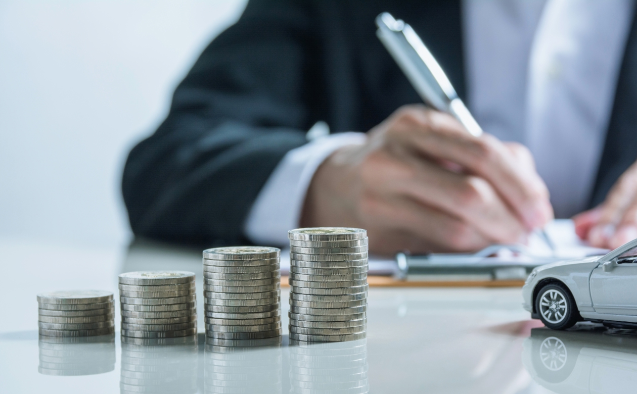 stablet mønter med lille bil ved siden af og mand der gennemgår kørselsgodtgørelse i baggrunden