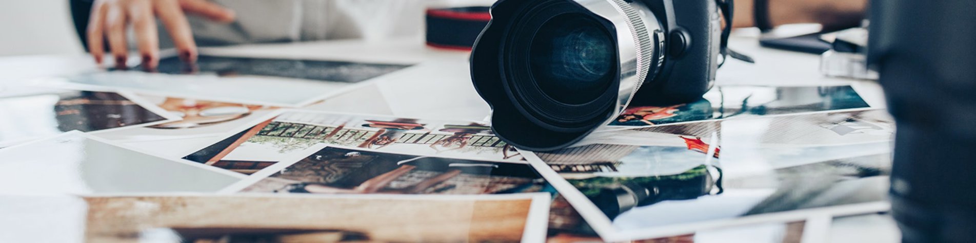 Fotograf sidder med en masse kommercielle personbilleder foran sig på et bord samt et kamera