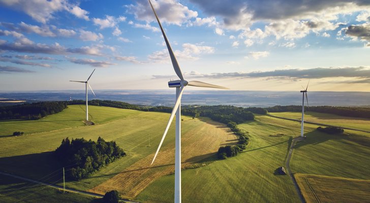 Tre vindmøller på grønne marker under blå himmel