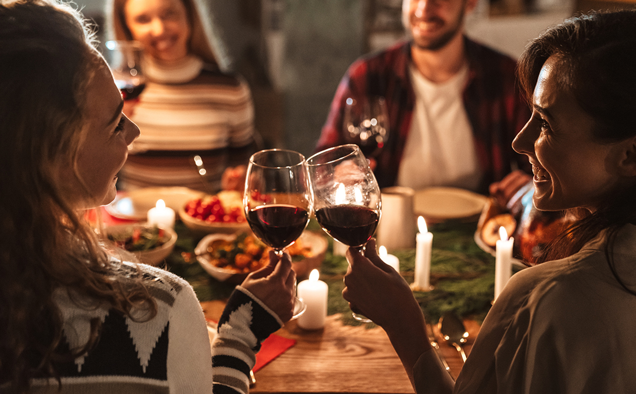 To kvinder skåler i vin til julefrokost med to personer siddende overfor dem