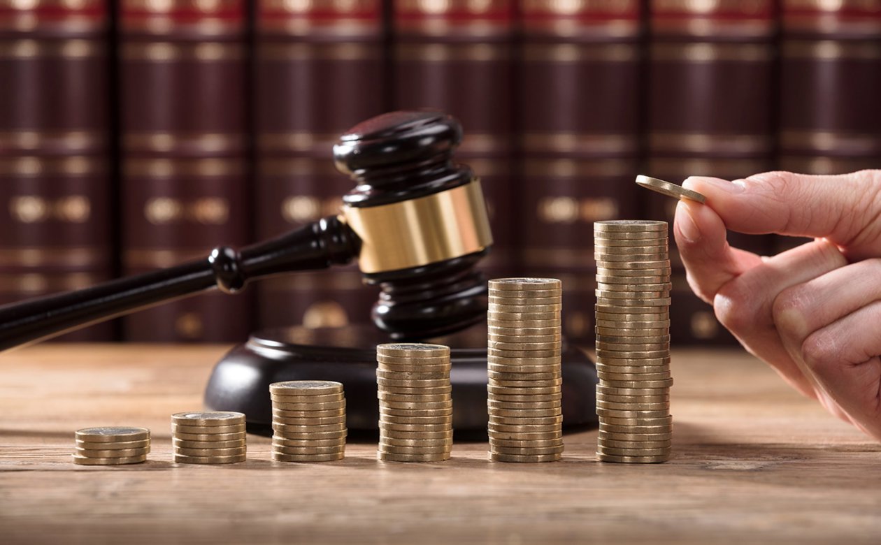 Hånd stabler mønter med dommerhammer bagved mønterne - kompensation 