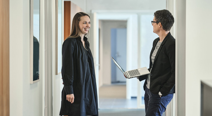Ditte Marie Hansen og Jeanette Dich Sørensen med bærbar i hånden står og taler sammen på gang