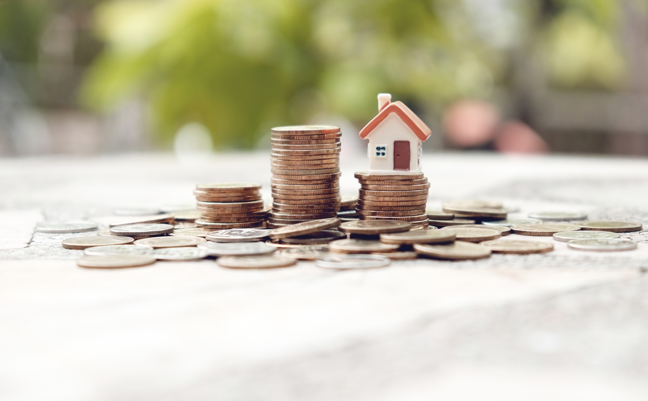 Stakke af mønter med et lille hus ovenpå og mønter rundt omkring