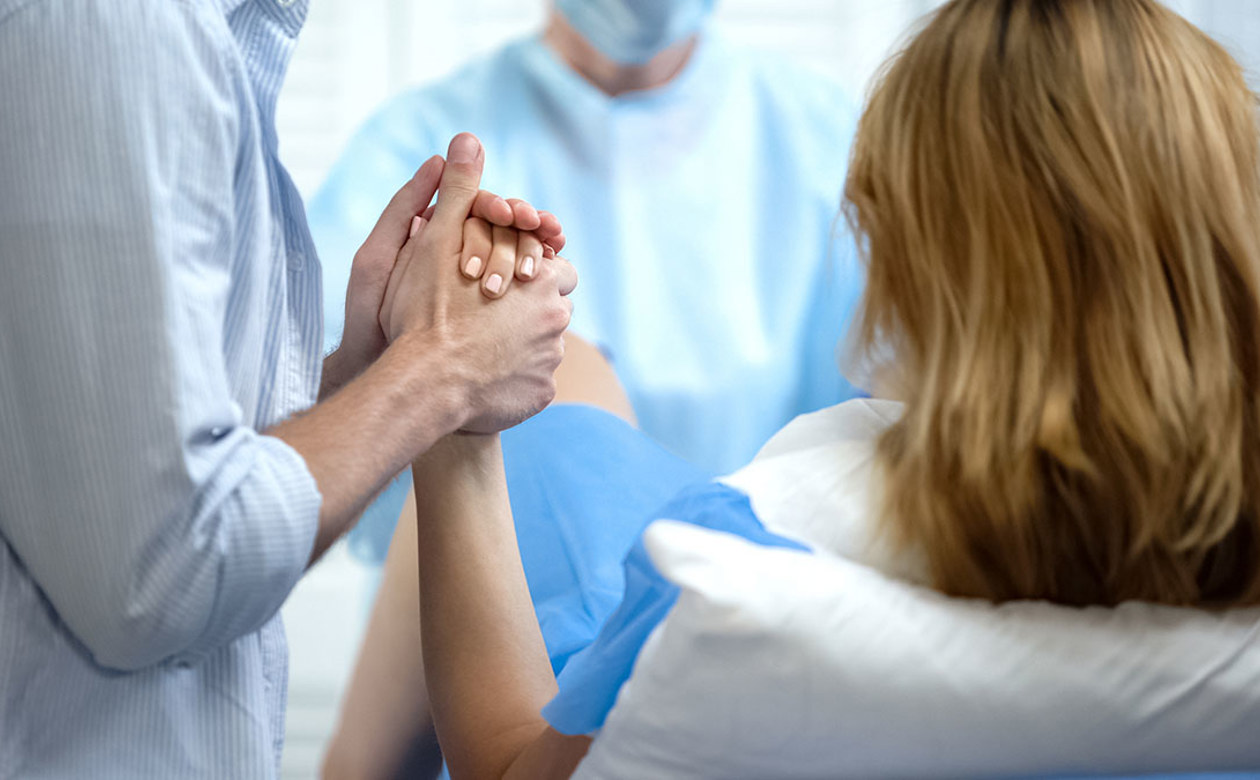 Kvinde i fødsel med sin mand i hånden og læge tilstede