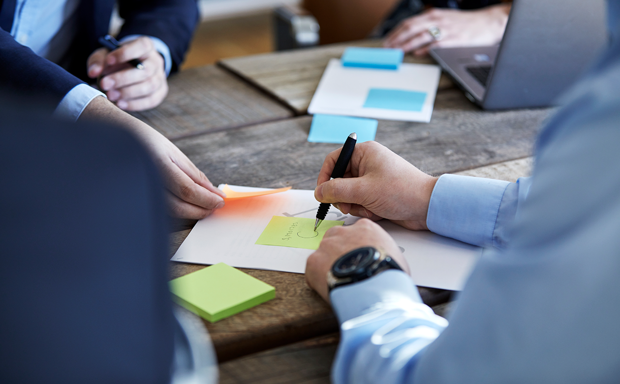 Møde mellem fire personer hvor der bliver skrevet på papir og post-it