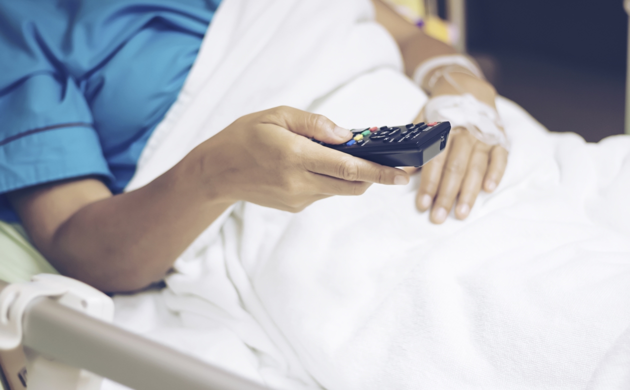 Person i hospitalsseng med fjernbetjening i hånden