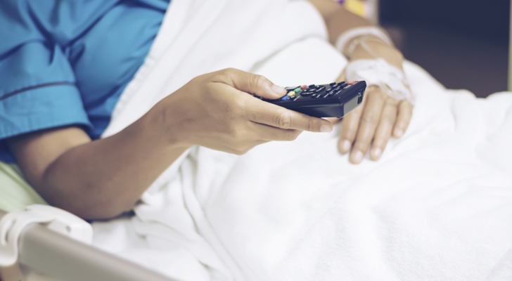 Person i hospitalsseng med fjernbetjening i hånden