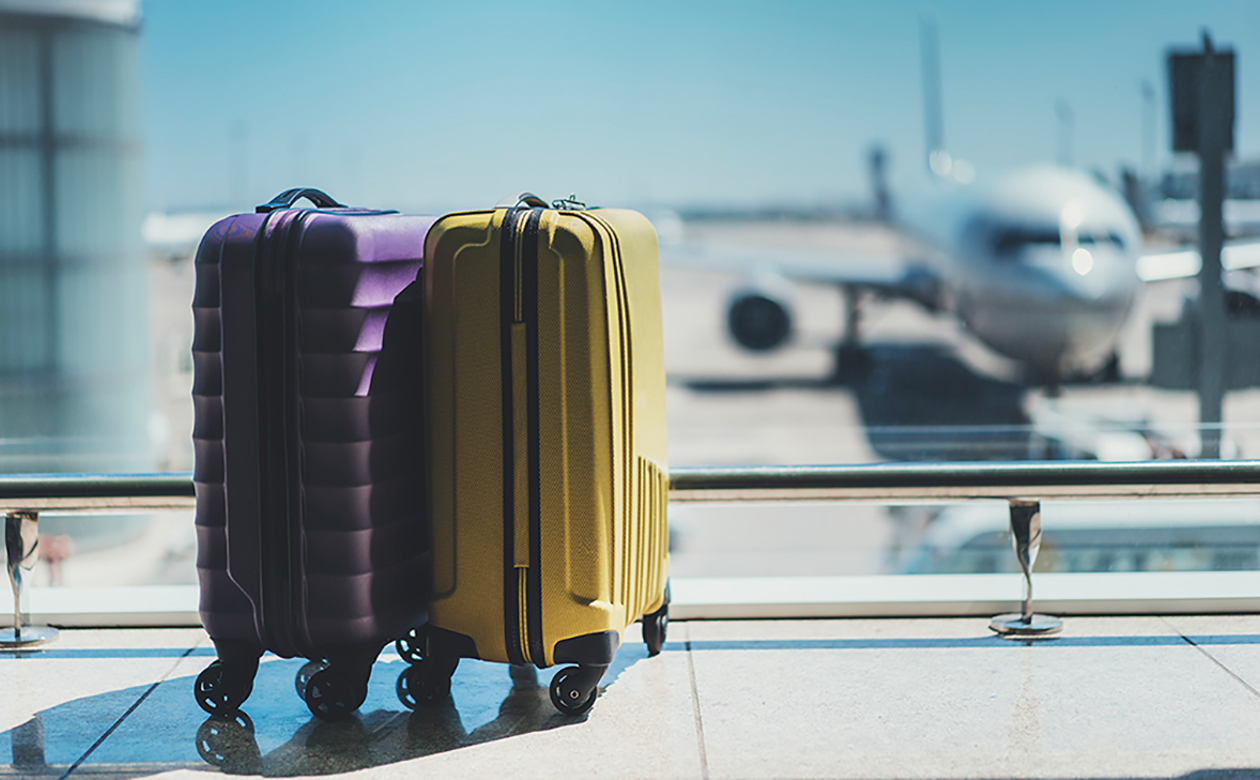 To kufferter i lufthavn med fly i baggrunden